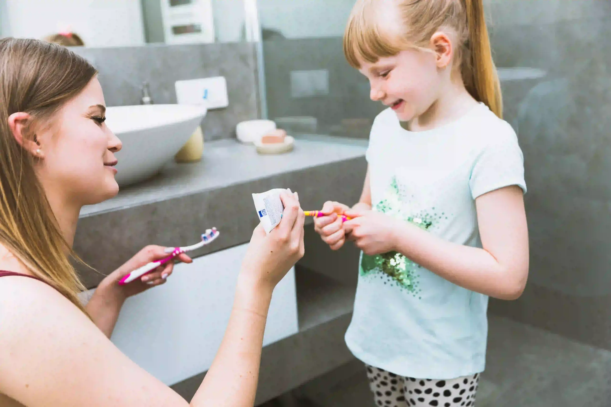 mother squeezing paste toothbrush daughter